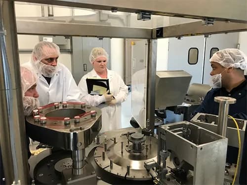 People wearing PPE surrounding an Index K120i capsule filling machine.