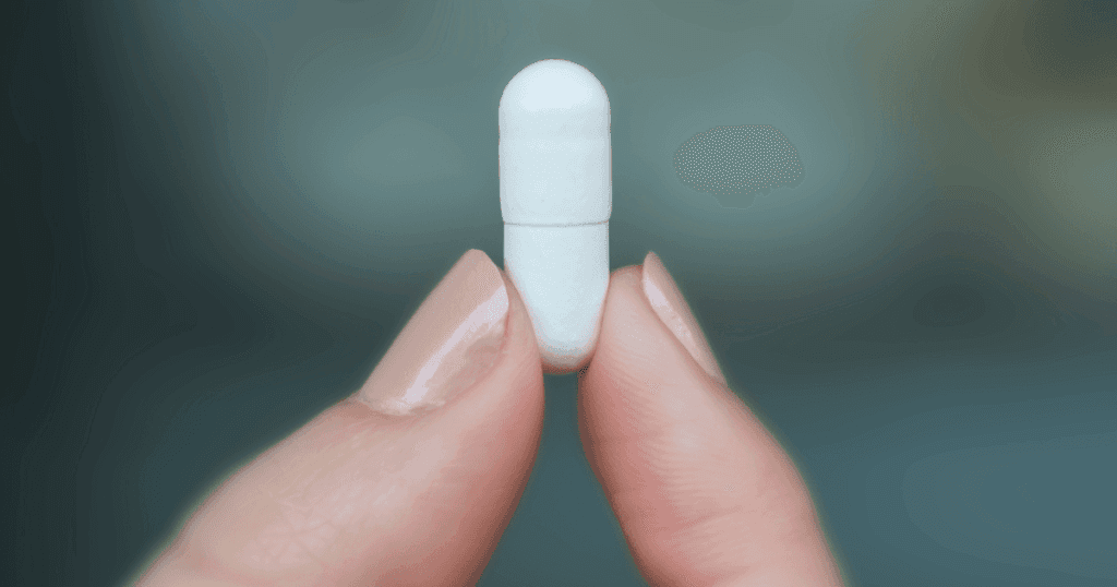 A close up shot of a person holding a white capsule, showing the capsule body and capsule cap.