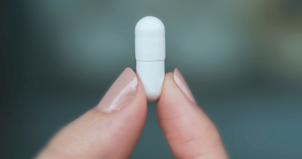 A close up shot of a person holding a white capsule, showing the capsule body and capsule cap.
