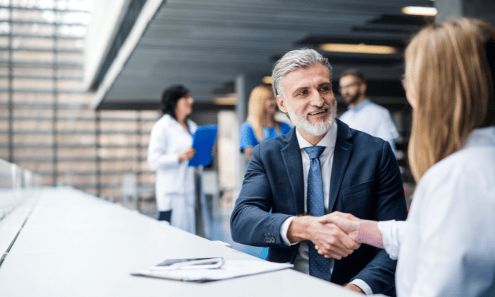 Grey-haired businessman in a suit shakes hands with a lab professional, symbolizing success in capsule filling technology.
