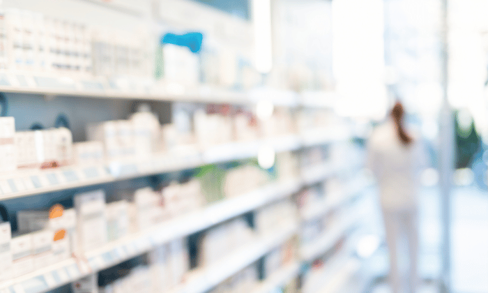 A blurry pharmacy aisle displays shelves of packaged medications, representing the final output from capsule fillers in pharmaceutical manufacturing.